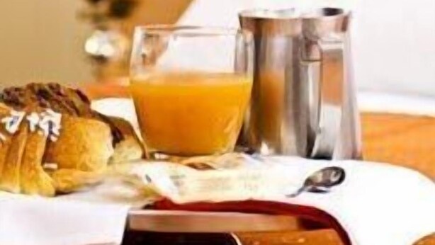 Une table mise pour le petit-déjeuner avec un croissant, un verre de jus d’orange et une carafe d’eau.