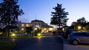A two-story building with a restaurant sign, parked cars, and a well-lit driveway at dusk. - Hotel Main Street (Rimini)