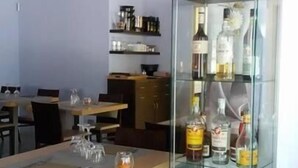 A dining area with a glass cabinet displaying bottles, a kitchen in the background, and a table set with a placemat and glasses. - Hotel Main Street (Rimini)