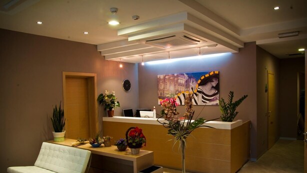 A reception area with a reception desk, two white cushioned chairs, a potted plant, and a painting on the wall. - Hotel Main Street (Rimini)