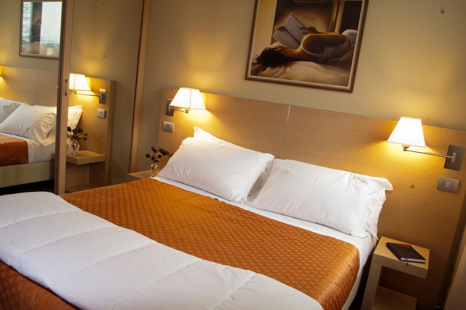 Une chambre d’hôtel avec un grand lit, deux lampes de chevet, une table de chevet, un miroir et un tableau au mur.