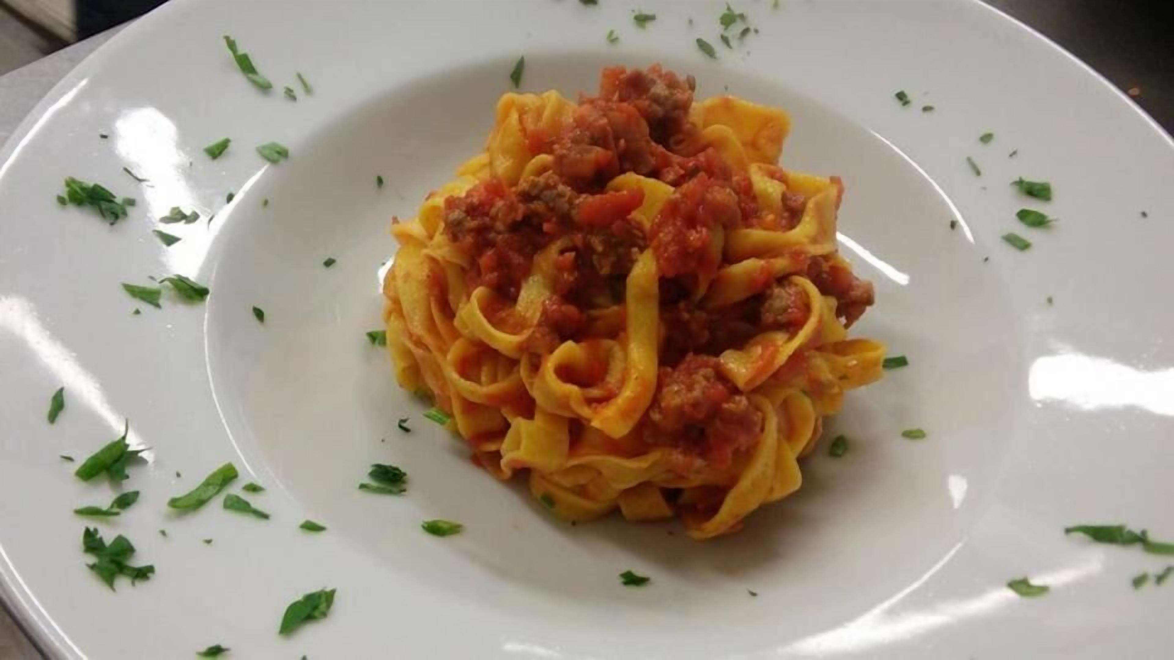 A plate of pasta with a tomato-based sauce and ground meat, garnished with chopped herbs.