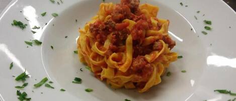 A plate of pasta with a tomato-based sauce and ground meat, garnished with chopped herbs.