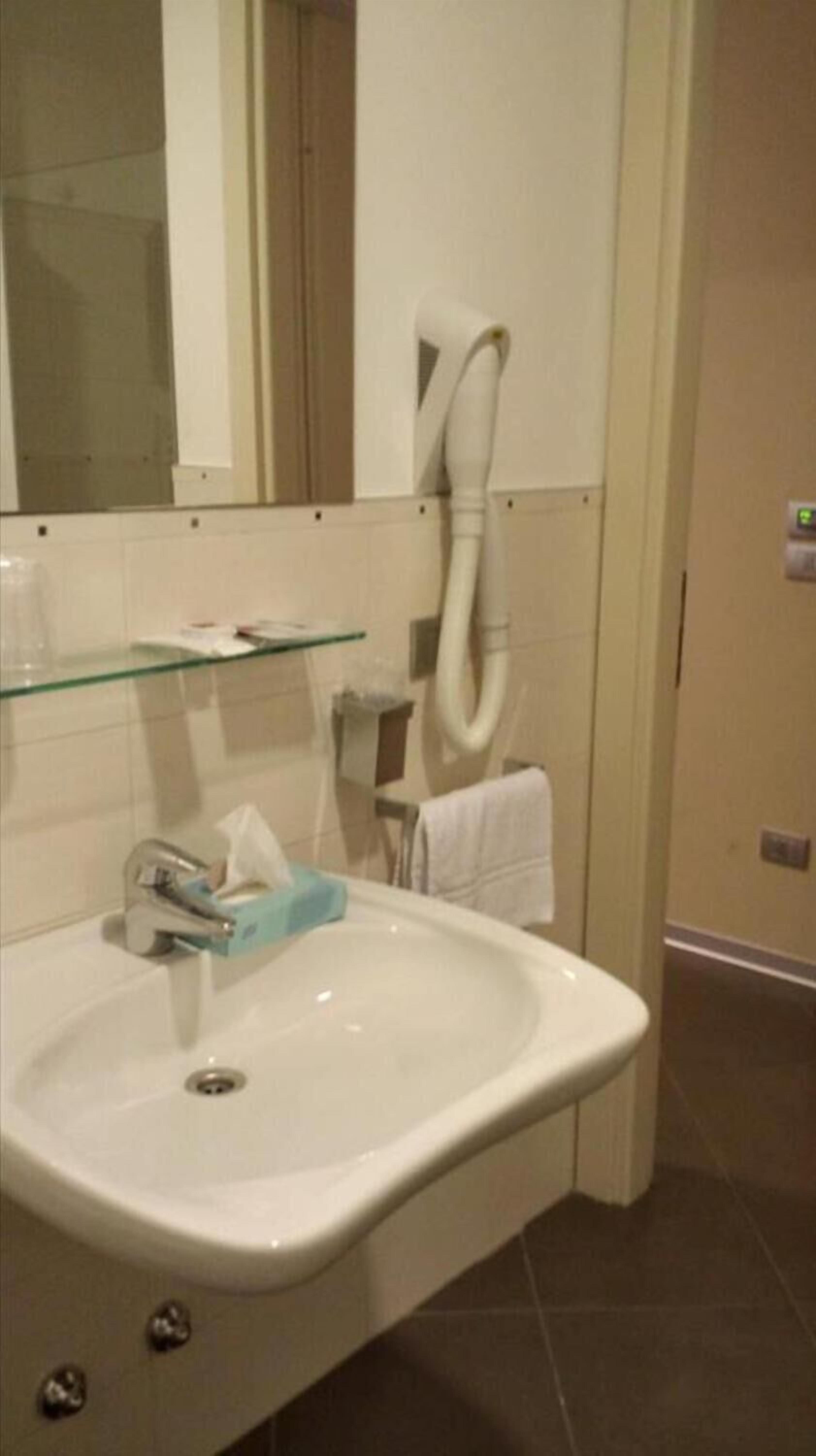 A bathroom with a white sink, a glass shelf, a towel rack, and a mirror.