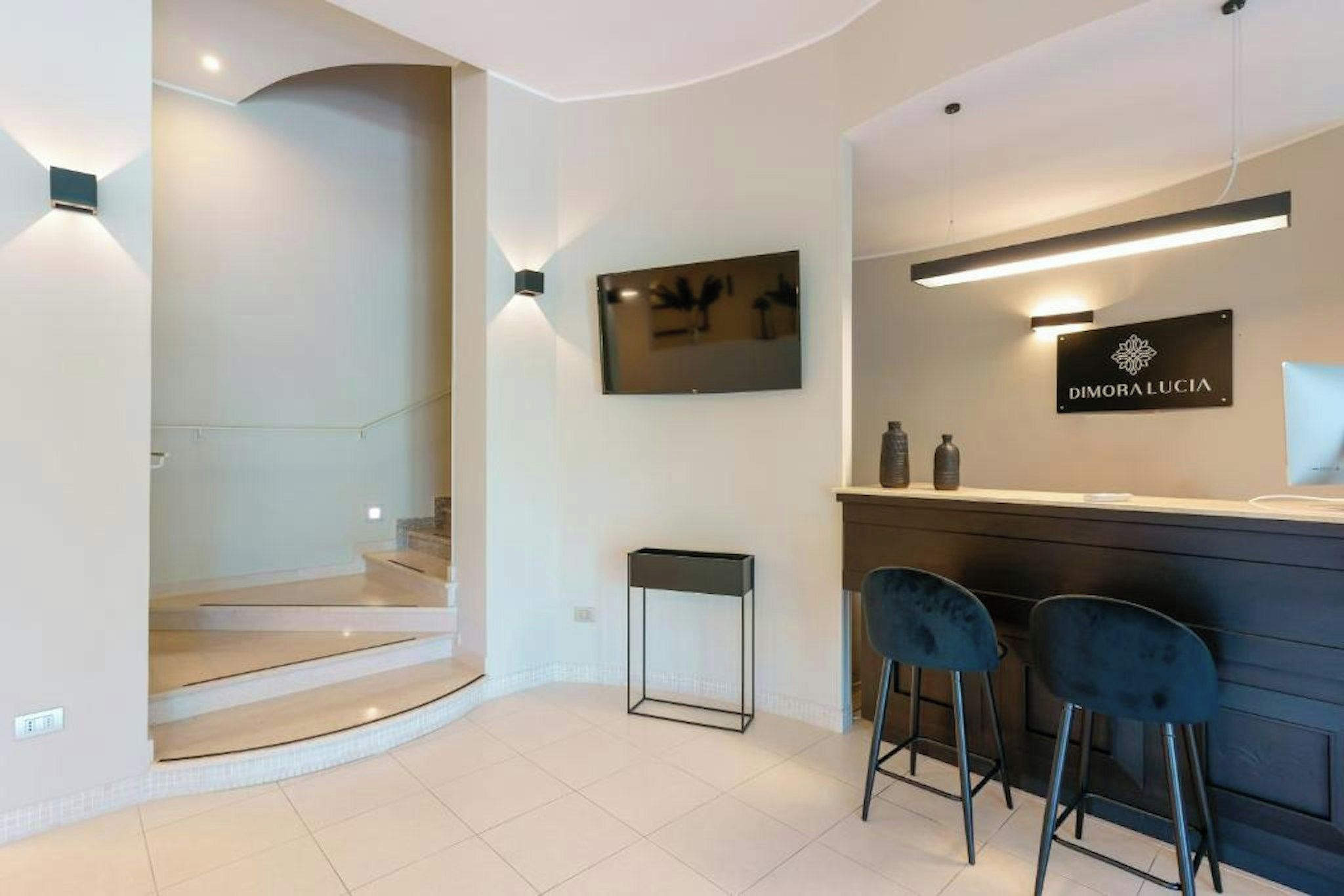 A modern interior with a staircase, a reception desk, and two bar stools.