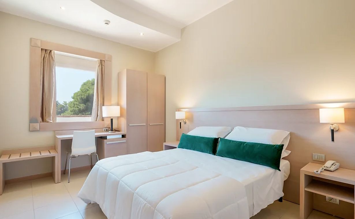 A hotel room with a bed, desk, chair, bedside tables, and a window with curtains.