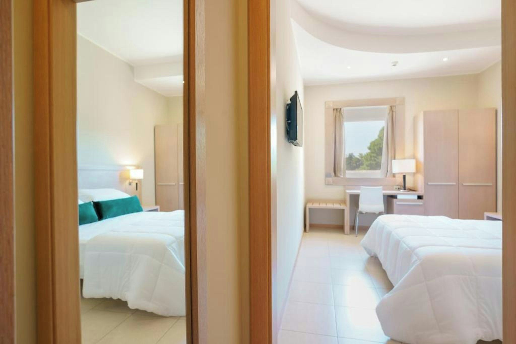 Habitación de hotel con dos camas, un escritorio, una silla, un televisor y un armario.