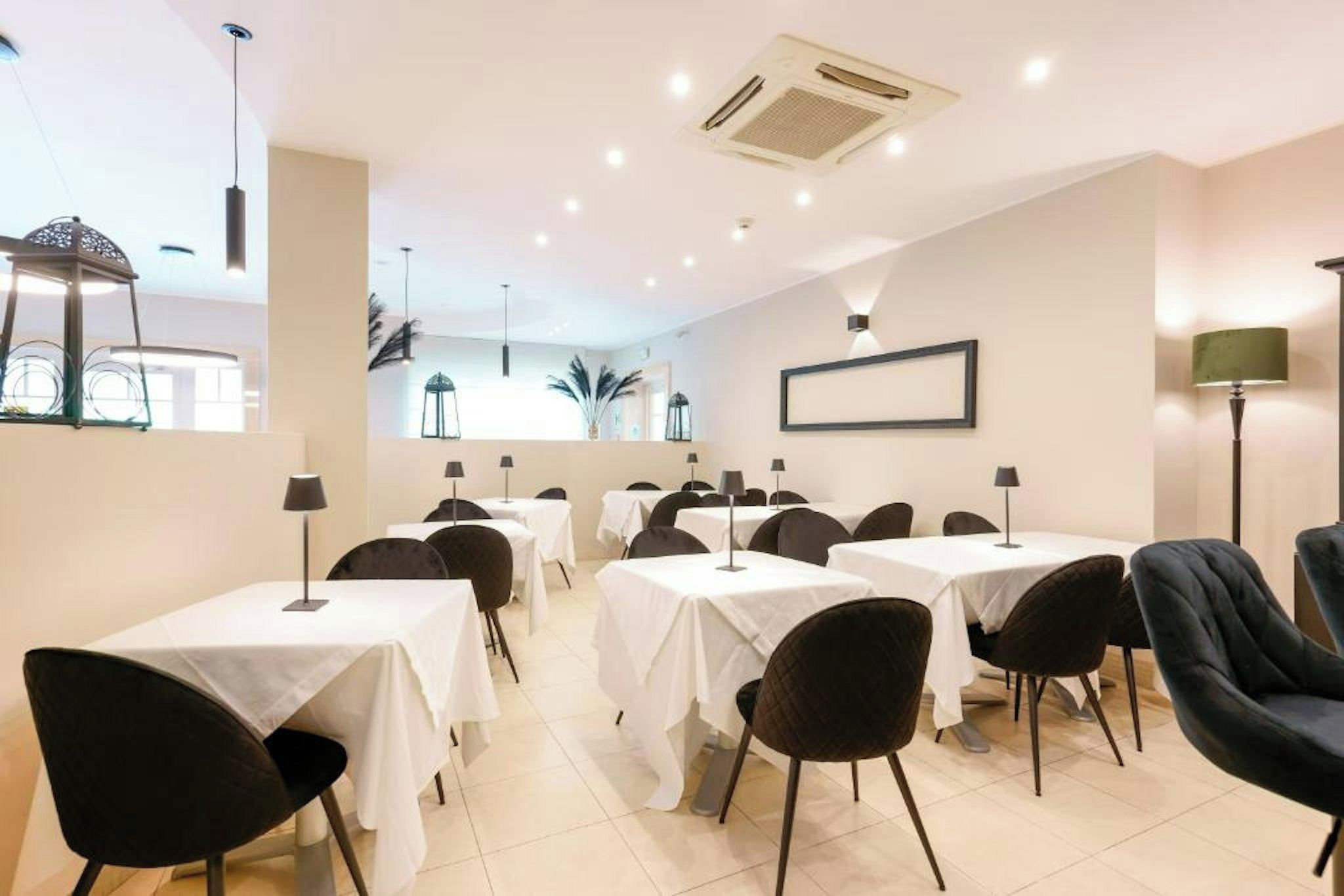A dining area with tables and chairs, air conditioning, and a framed picture on the wall.