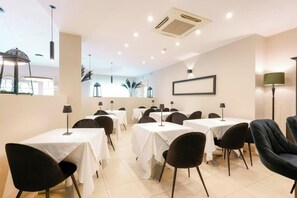 Uma sala de jantar com mesas e cadeiras, ar condicionado e um quadro na parede.