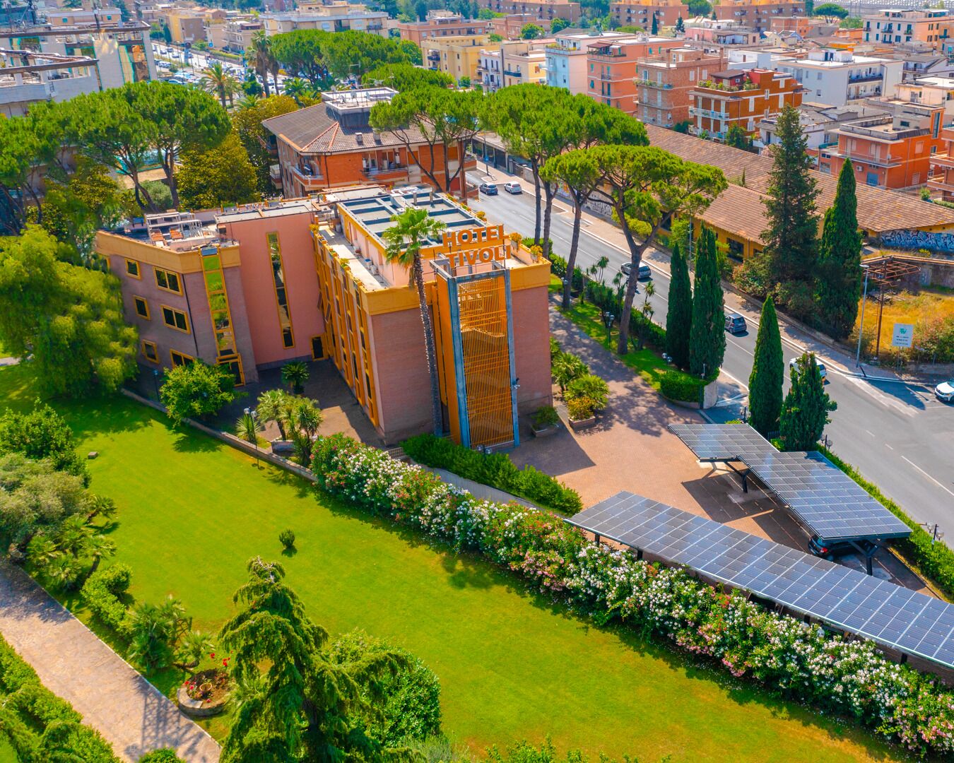 Un hotel de diseño moderno, con una terraza en la azotea que cuenta con paneles solares, rodeado de abundante vegetación y un jardín cuidado.