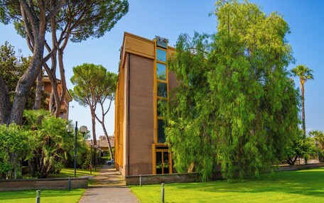 A modern building with a glass facade, surrounded by lush greenery and trees.
