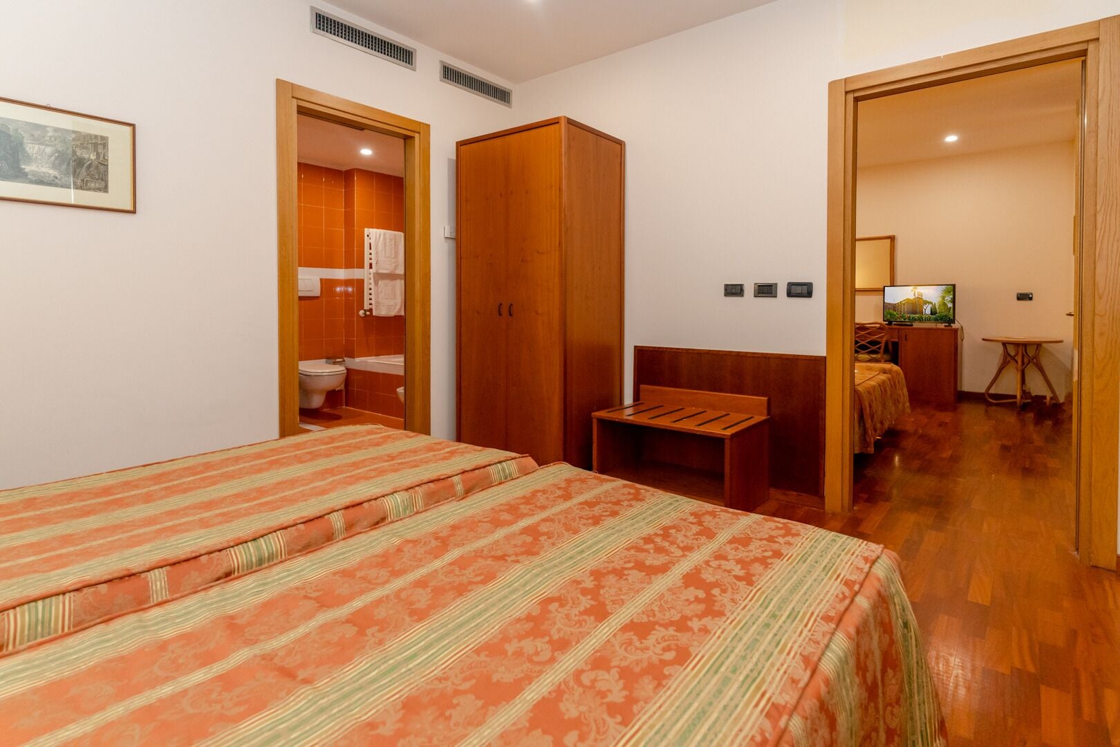 A bedroom with two beds, a wooden wardrobe, a small table, and a television.