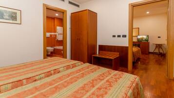 A bedroom with two beds, a wooden wardrobe, a small table, and a television.