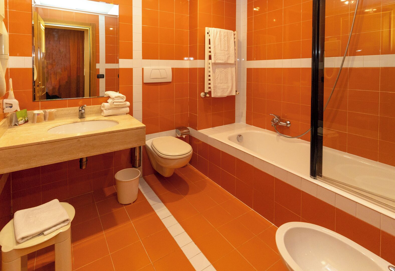 A bathroom with orange tiles, a sink, a toilet, a bathtub, and a shower.