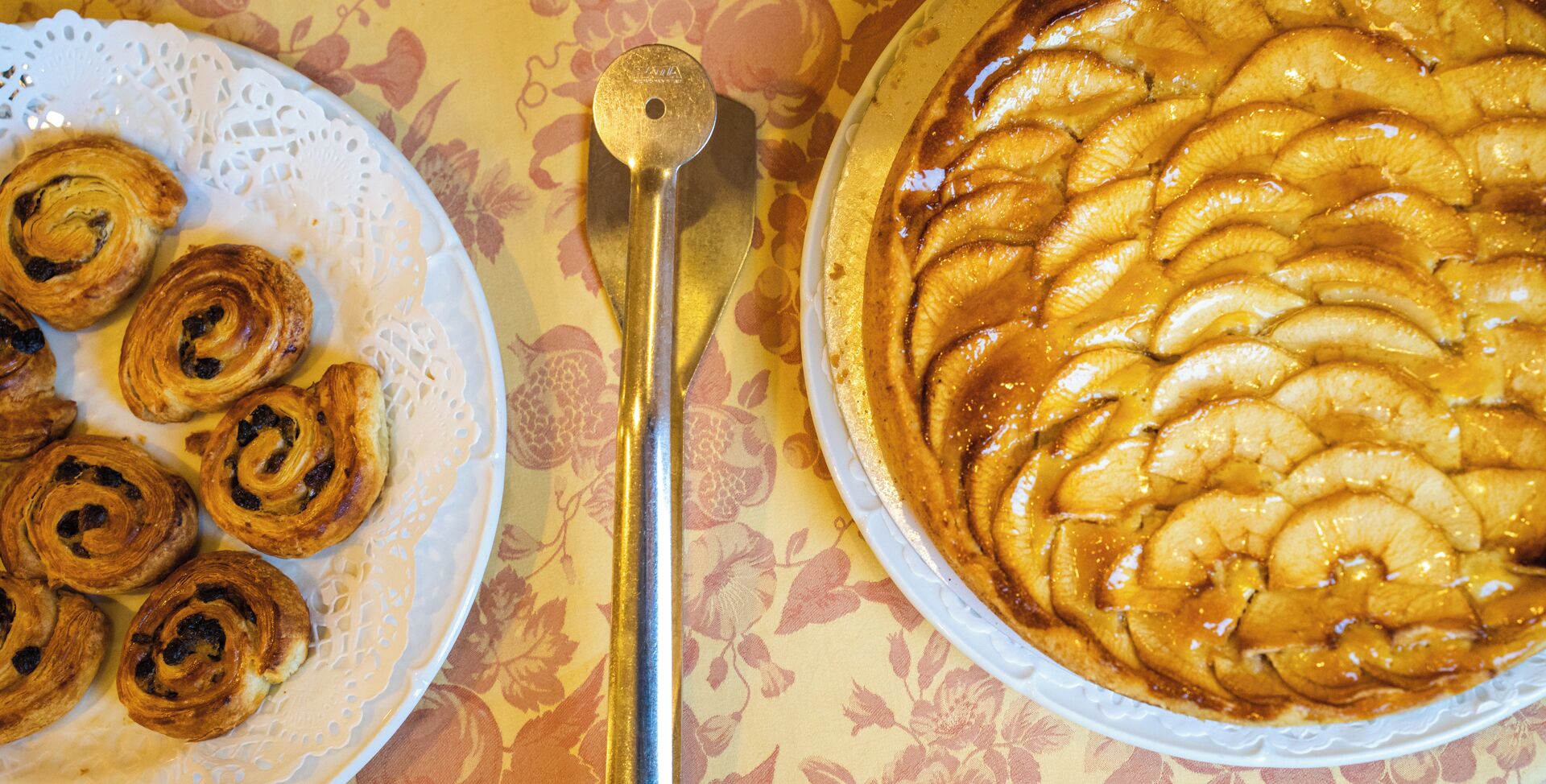 Un plato de pasteles y una tarta de frutas sobre una mesa con mantel floreado.