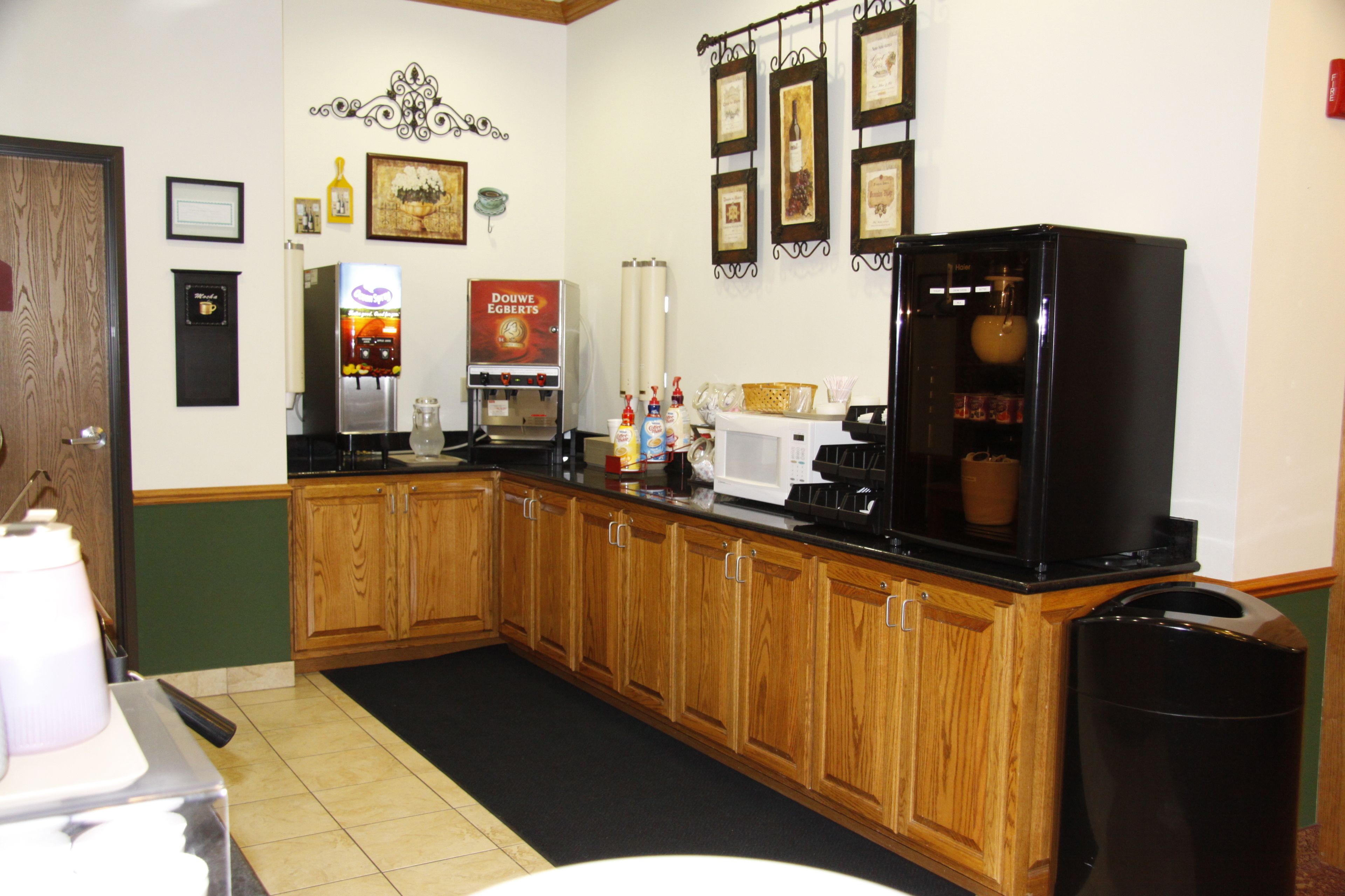 A kitchen with wooden cabinets, a coffee machine, a microwave, and a trash can.
