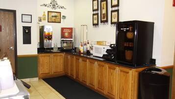 A kitchen with wooden cabinets, a coffee machine, a microwave, and a trash can.