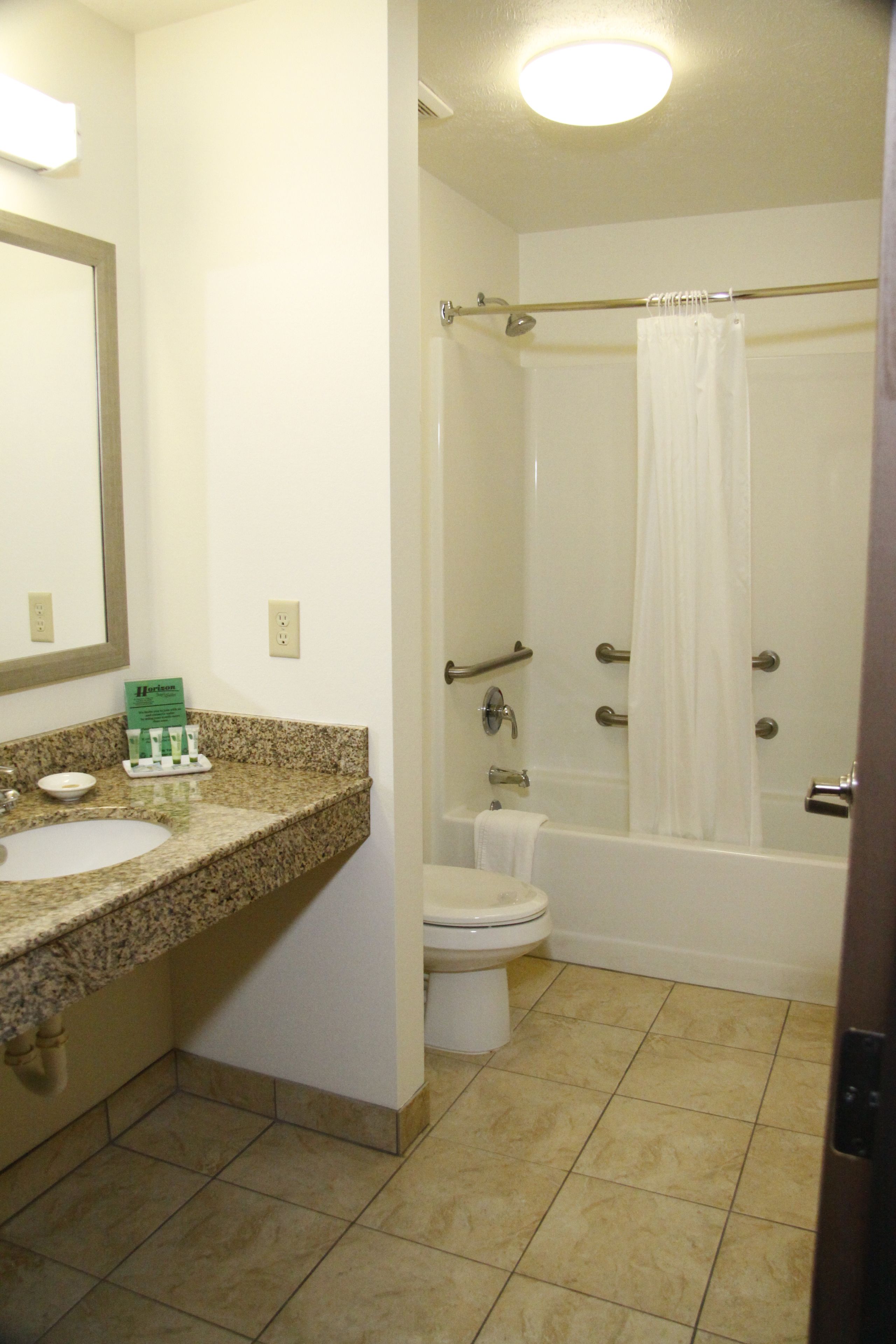 A bathroom with a granite countertop, a sink, a toilet, and a bathtub with a shower curtain.