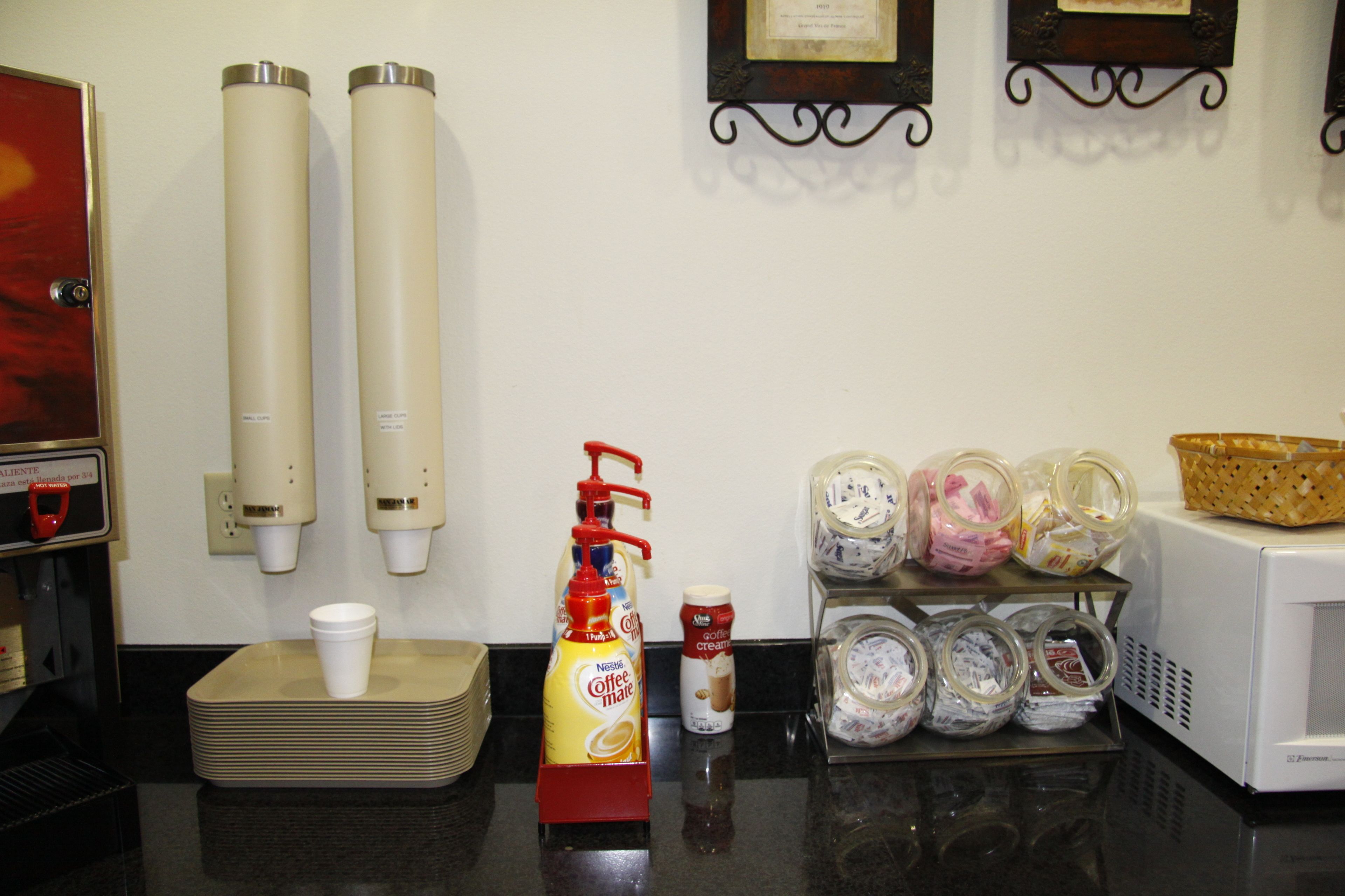 Una estación de café con dispensador, tazas y cafetera.