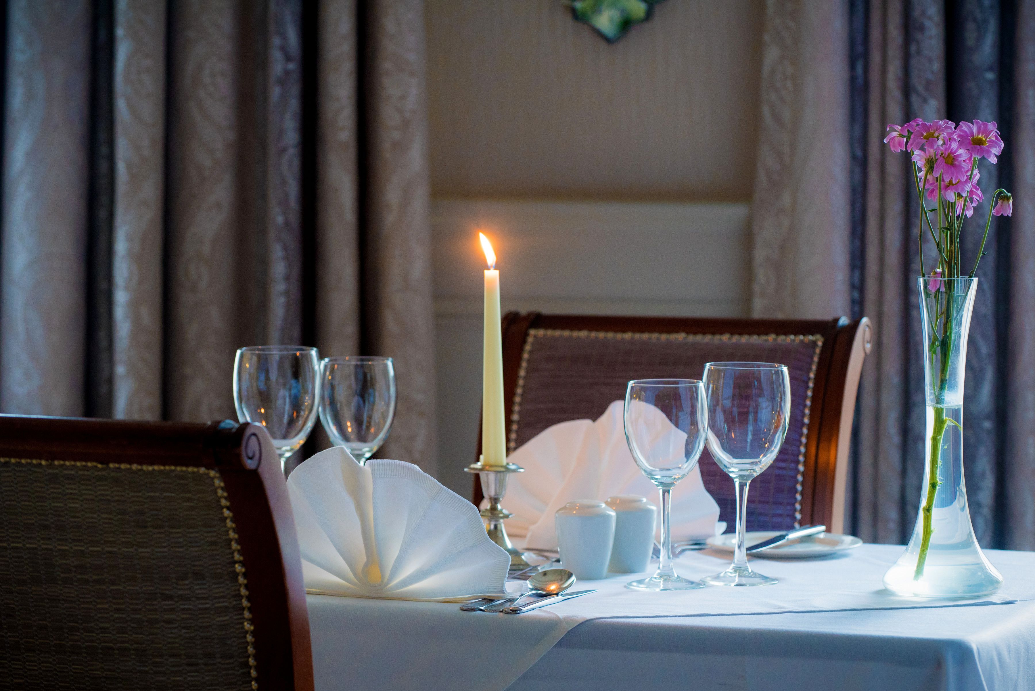 A table set for dining with a candle, glasses, a vase with flowers, and a folded napkin.
