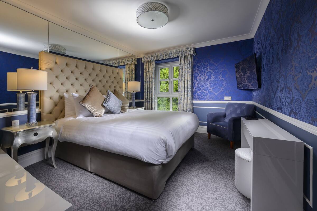 Ein Schlafzimmer mit einem großen Bett, einem Nachttisch mit Lampen, einem Sessel und einem an der Wand befestigten Fernseher.