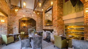 Een restaurant met bakstenen muren, houten balken en hangende lampen. Tafels en stoelen staan klaar voor het diner.