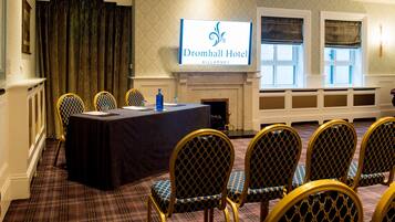 A conference room at Dromhall Hotel with a long table, chairs, a fireplace, and a large screen displaying the hotel name.