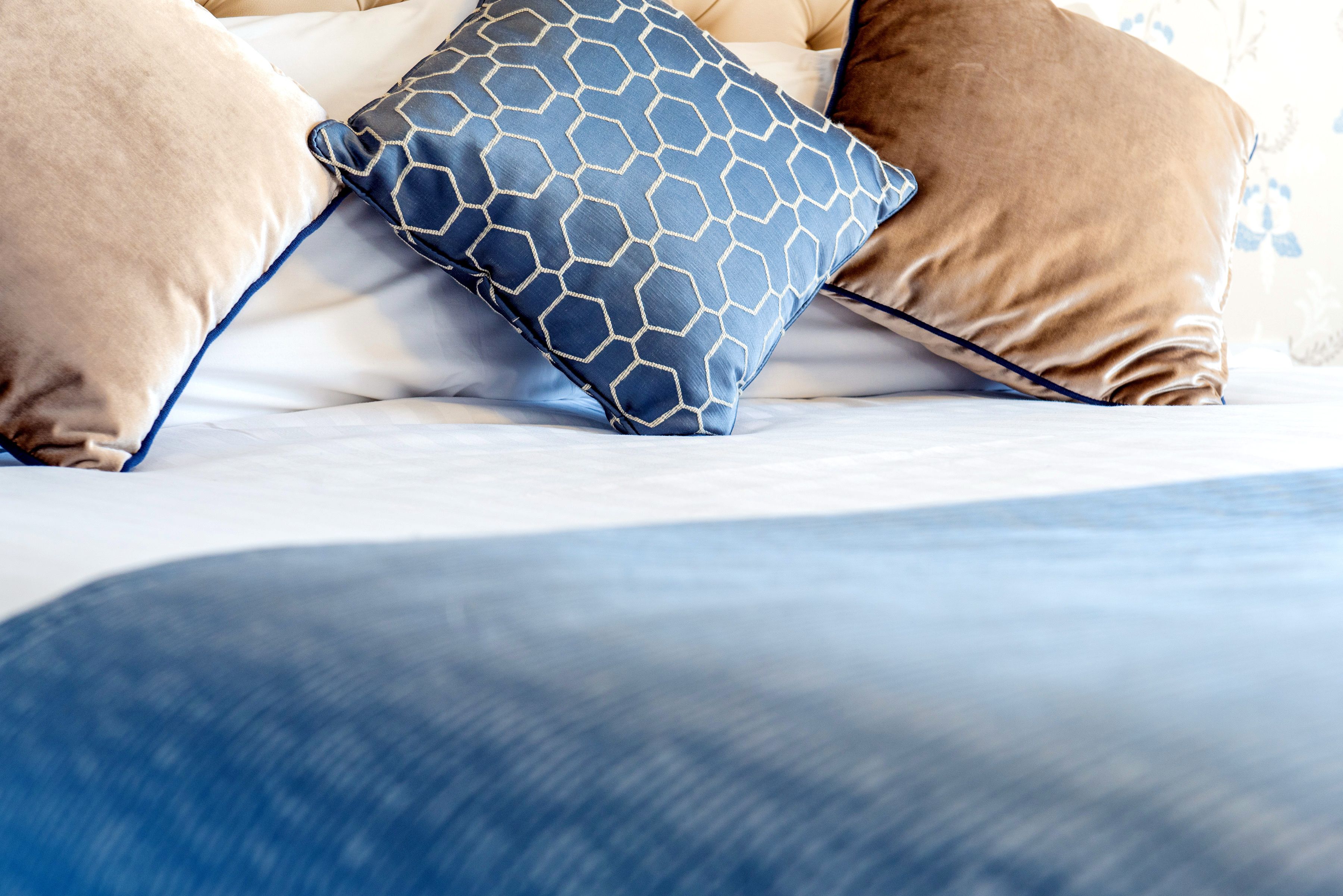 A bed with a blue and brown patterned pillow and a blue blanket.