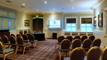 A conference room with a long table, chairs, a fireplace, and a screen displaying the hotel name.