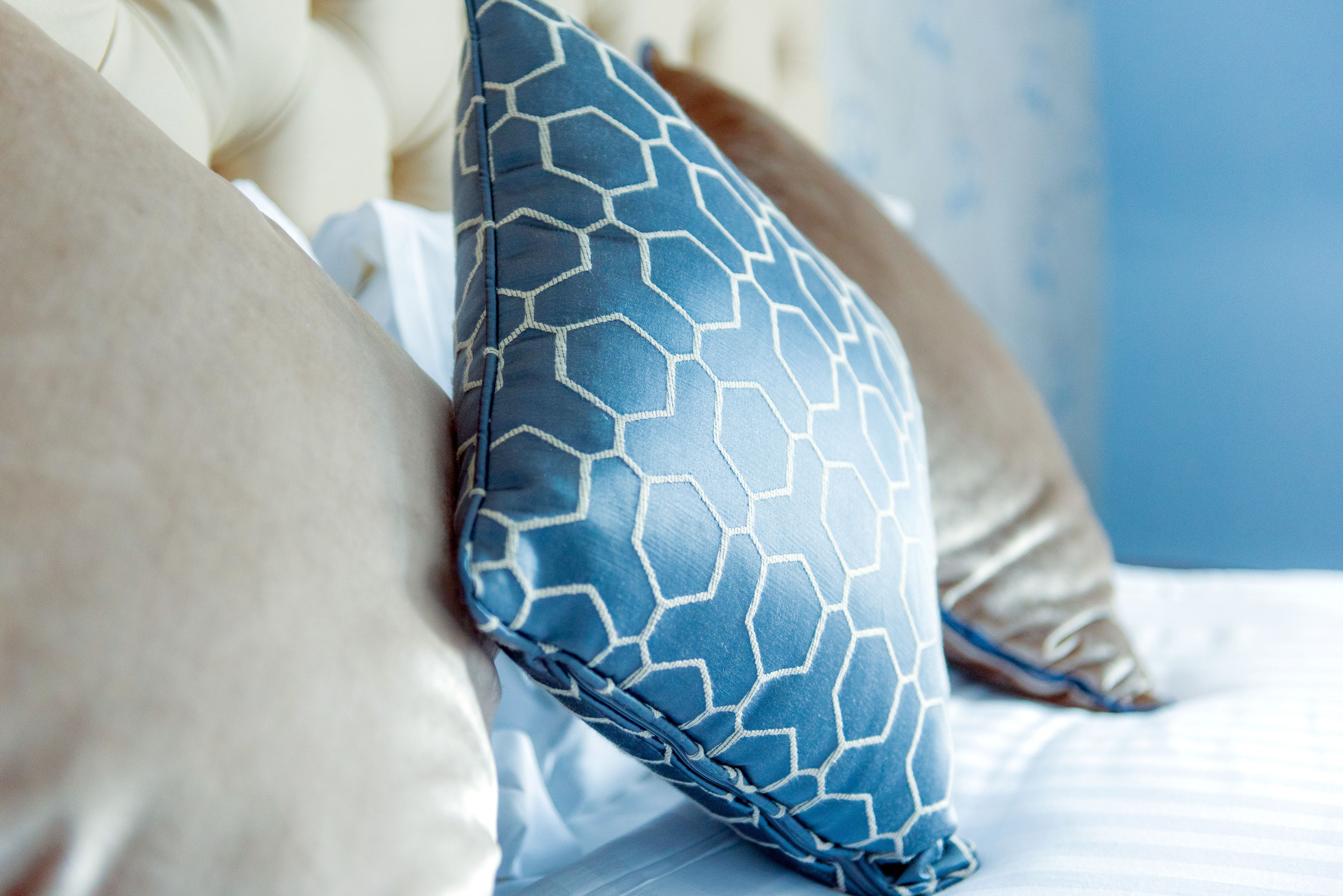 A close-up of a bed with a blue patterned pillow and a beige pillow.