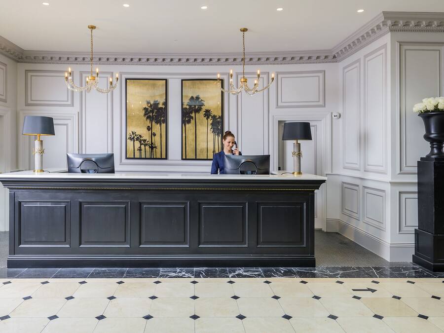 A spacious lobby with a large dark-colored reception desk, two wall-mounted lamps, and a chandelier.