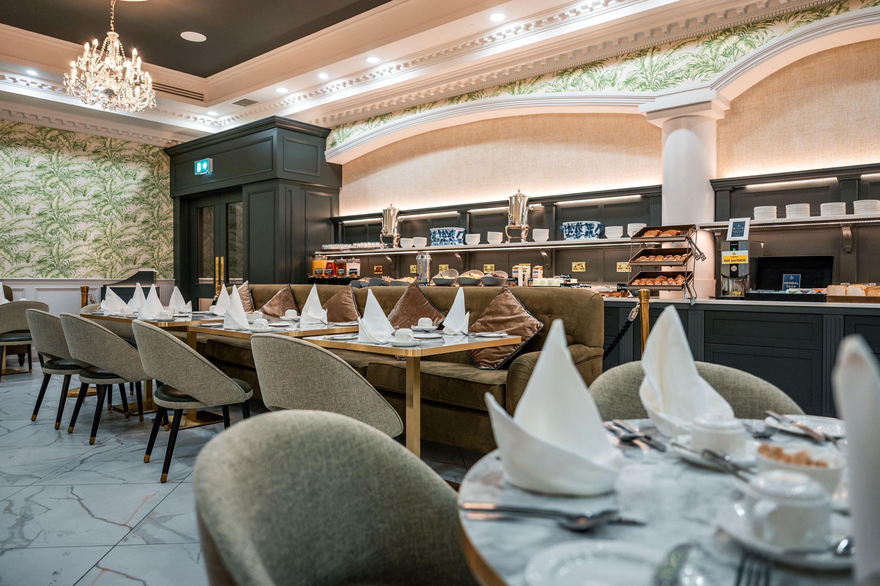 Un restaurante con piso de mármol, asientos acolchados y una zona de bufé con bandejas de comida.