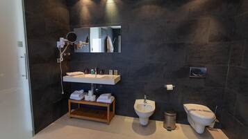 Une salle de bain moderne avec des murs recouverts de carreaux foncés, un meuble-lavabo en bois, un bidet et des toilettes.