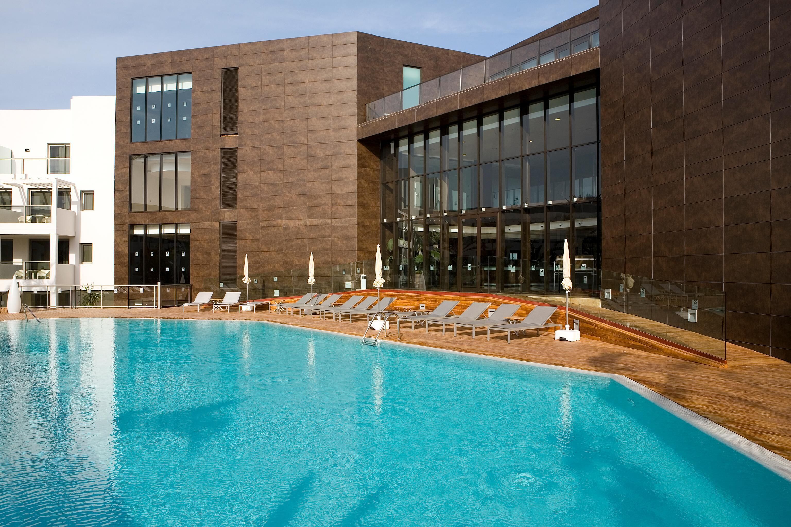 Een modern gebouw met een zwembad, ligbedden en een houten terras.