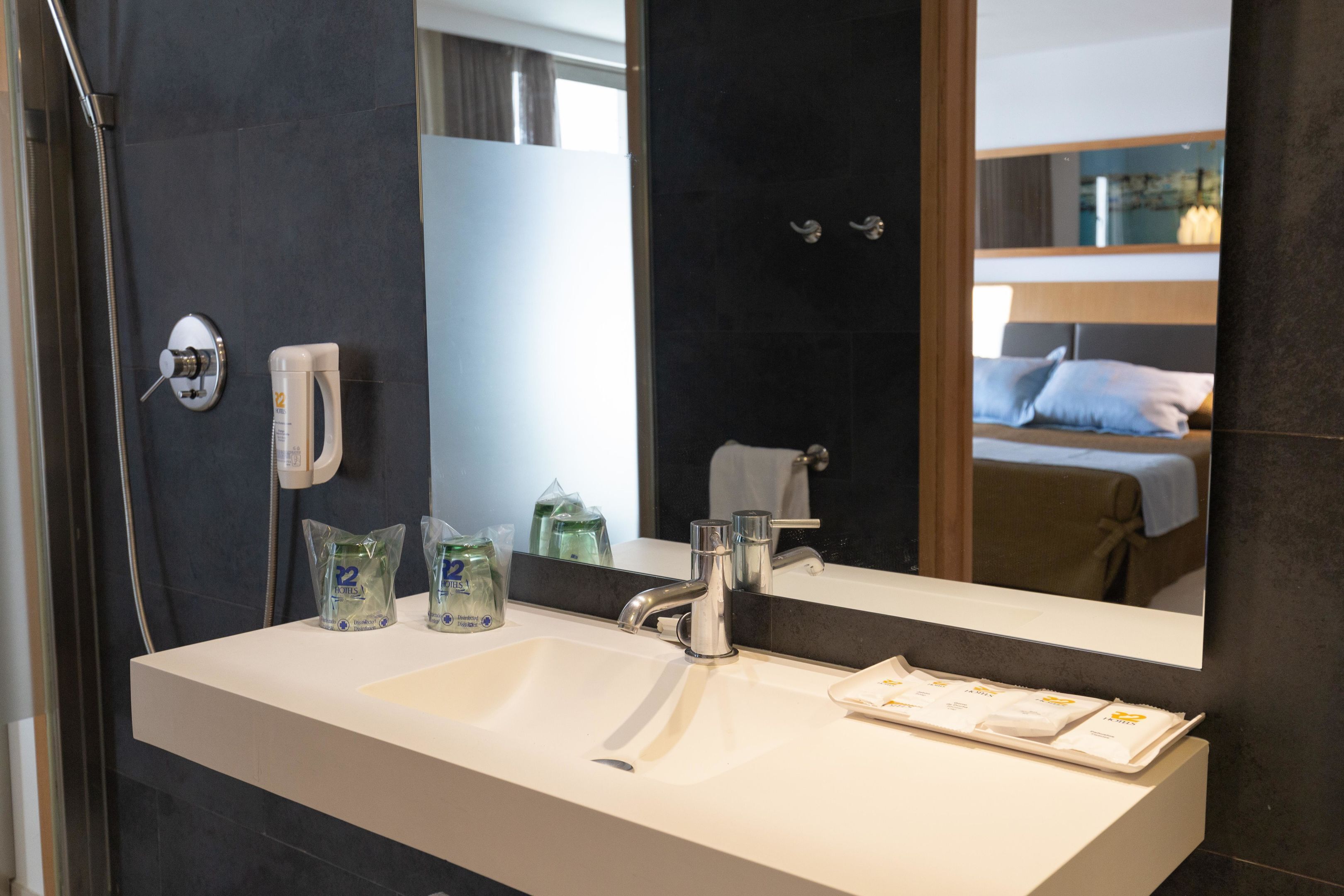 A hotel bathroom with a large mirror, a sink, and toiletries.