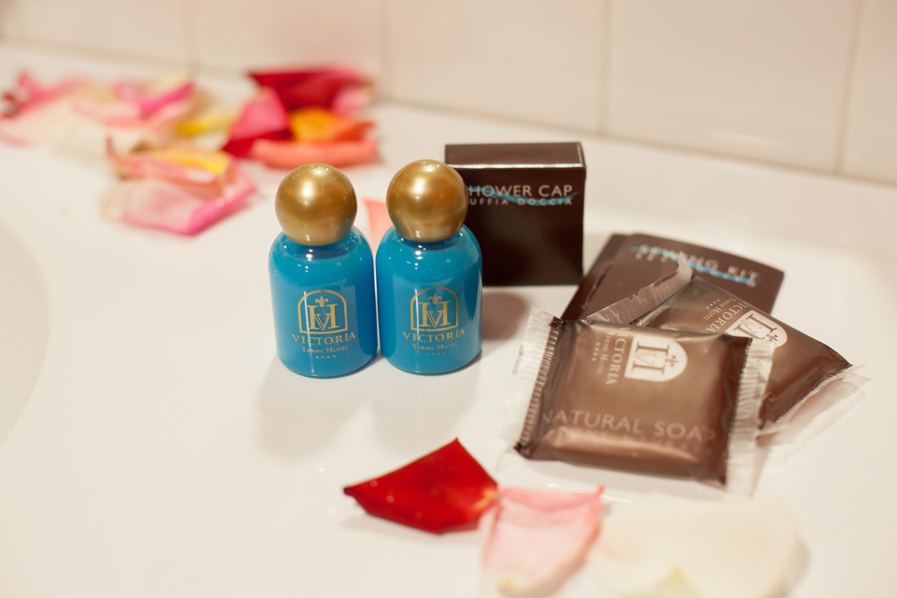 A bathroom with a shower cap, natural soap, and two bottles of Victoria hotel body wash.