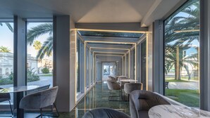 A modern interior with a long corridor, seating areas, and large windows offering views of palm trees and a building. - Victoria Terme Hotel (Tivoli)