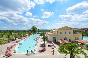 A large swimming pool with lounge chairs and umbrellas, surrounded by palm trees and a building with arched windows. - Victoria Terme Hotel (Tivoli)
