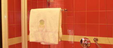 A bathroom with a glass-enclosed shower, a white bathtub, and red tiled walls.