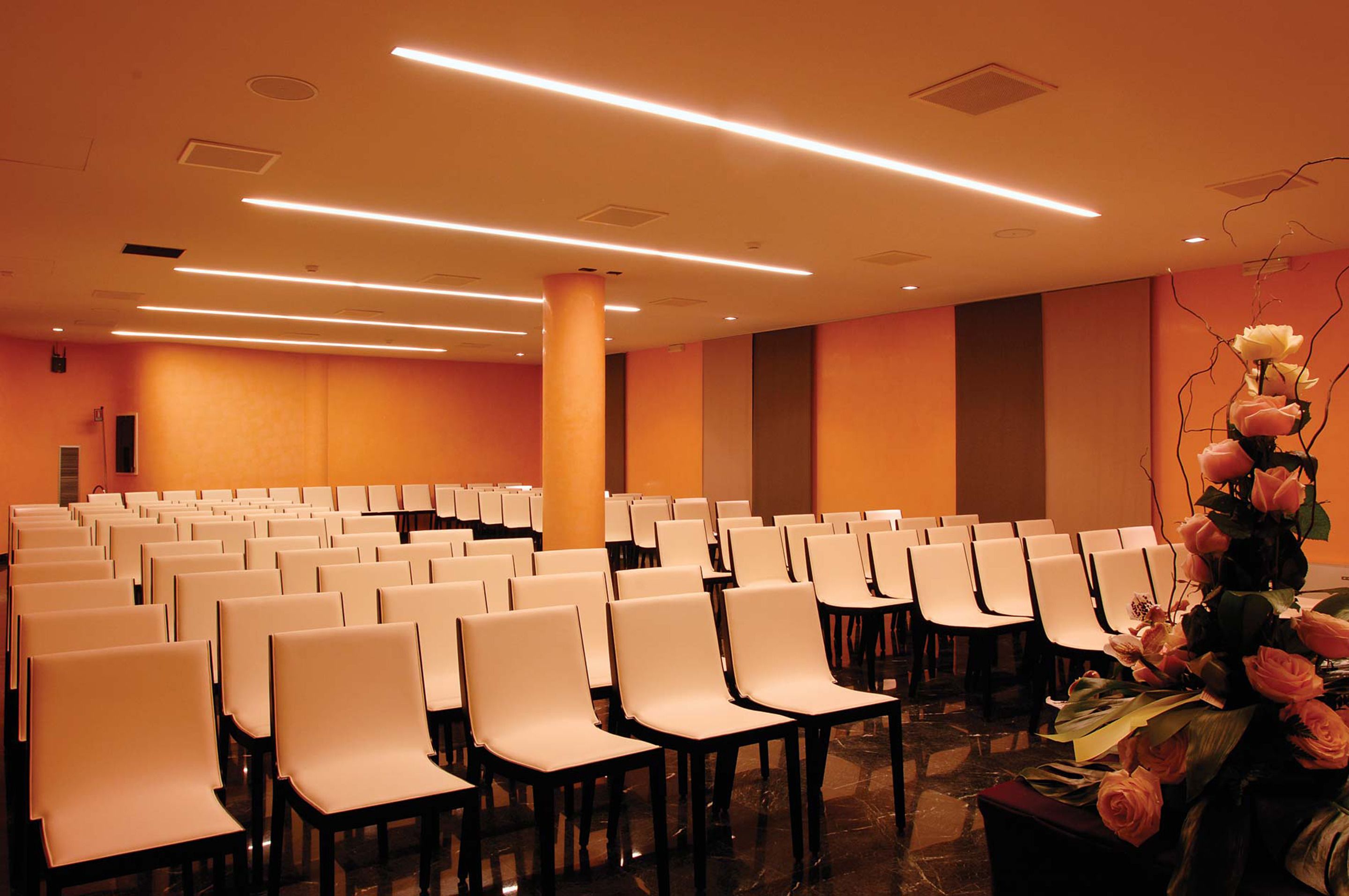 A conference room with rows of white chairs, a large pillar, and a floral arrangement on a table.