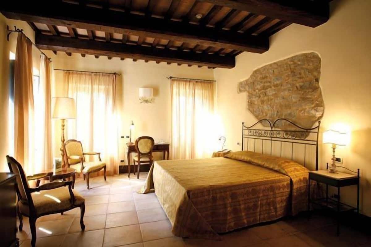 Une chambre d’hôtel avec un lit, deux chaises, un bureau et un mur en pierre.