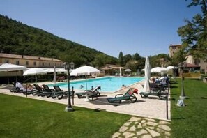 A pool area with lounge chairs and umbrellas, surrounded by a stone pathway and greenery.