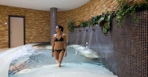 A woman walking in a spa area with a hot tub and a tiled wall with plants. - Borgo Hotel Le Terre del Verde (Gualdo Tadino)