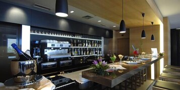 Una zona de bar moderna con una barra larga, máquinas de café espresso y una gran variedad de botellas.