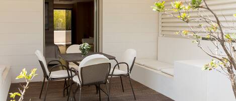 An outdoor patio with a table and chairs, a small plant, and a white wall.