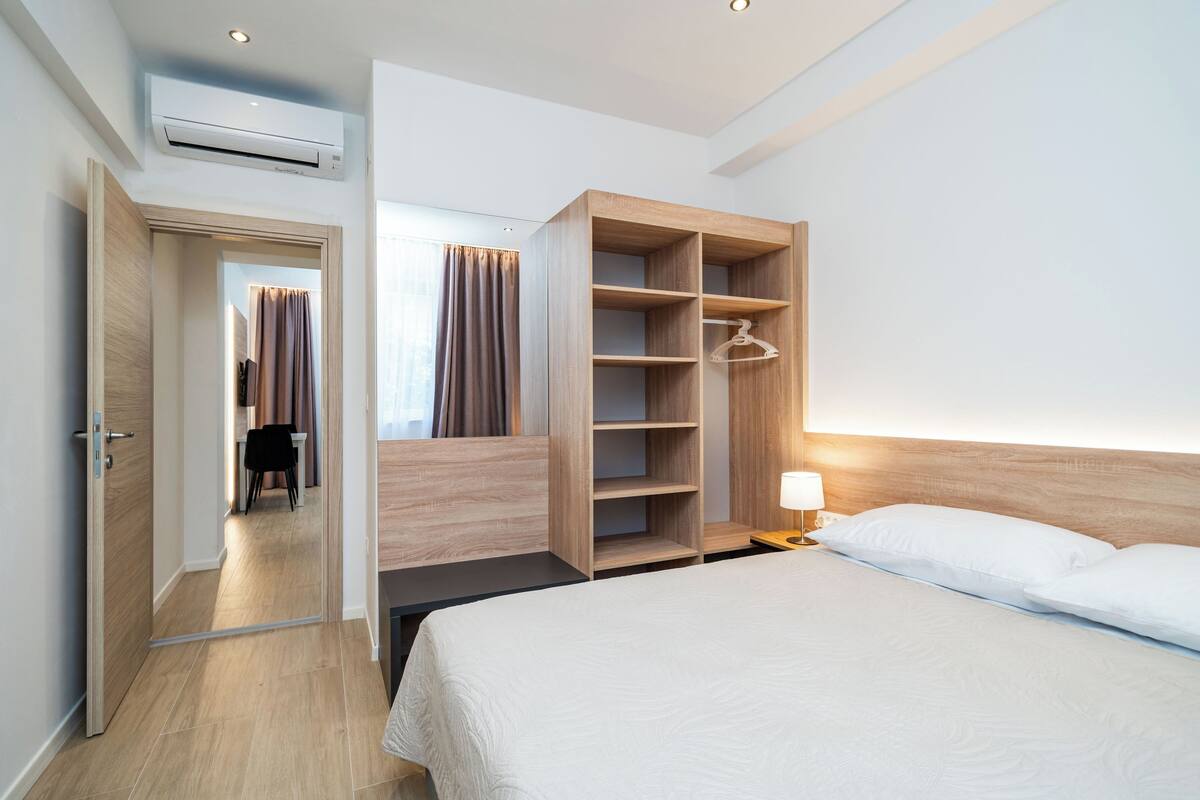 Habitación de hotel con cama, armario con varias repisas, espejo y equipo de aire acondicionado.