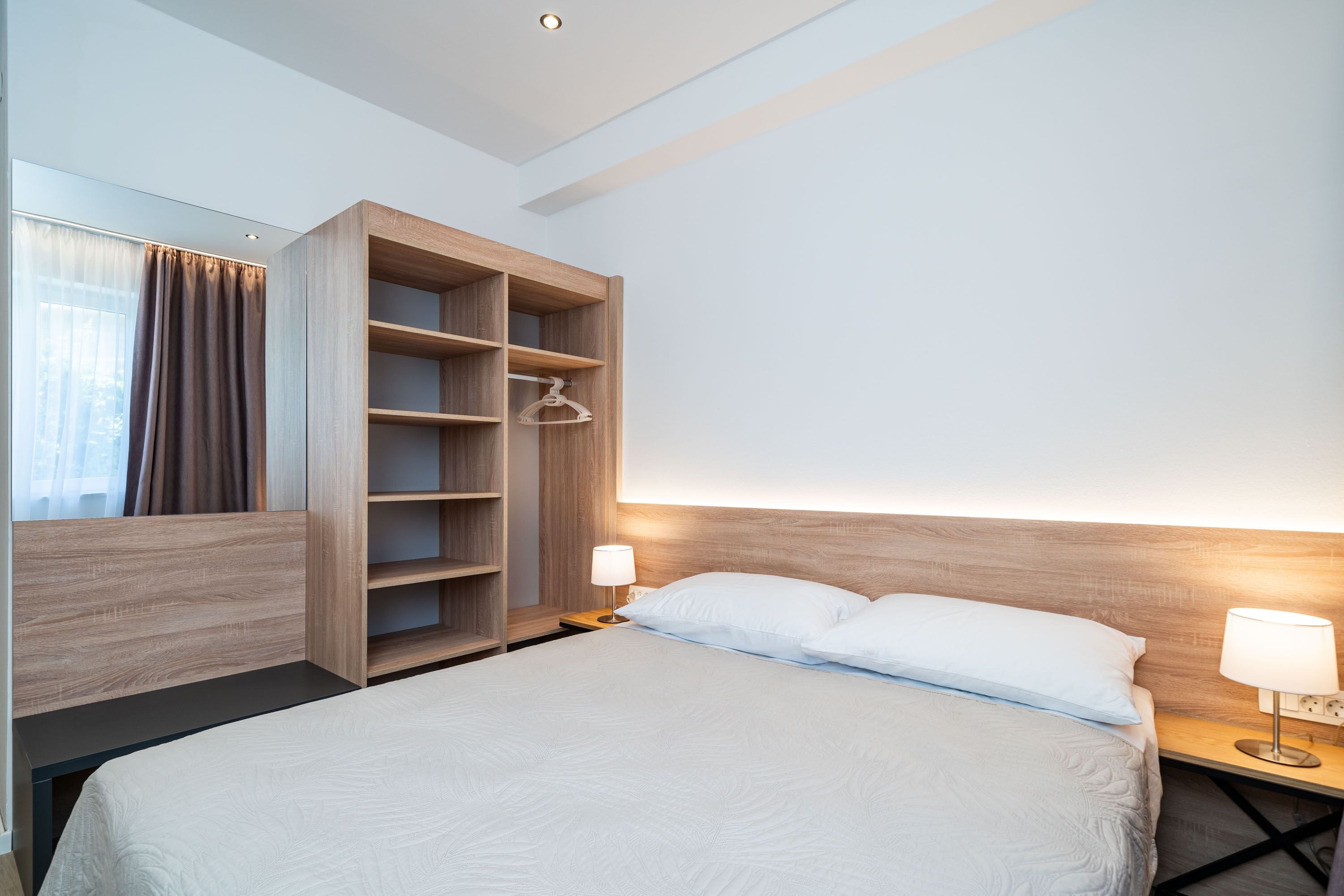 Una habitación de hotel moderna con una cama grande, un armario de madera y una mesita de noche con lámpara.
