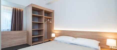 Una habitación de hotel moderna con una cama grande, un armario de madera y una mesita de noche con lámpara.