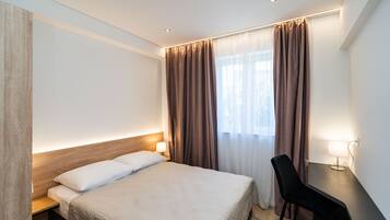 Een hotelkamer met een groot bed, een bureau met stoel, een lamp en een raam met gordijnen.