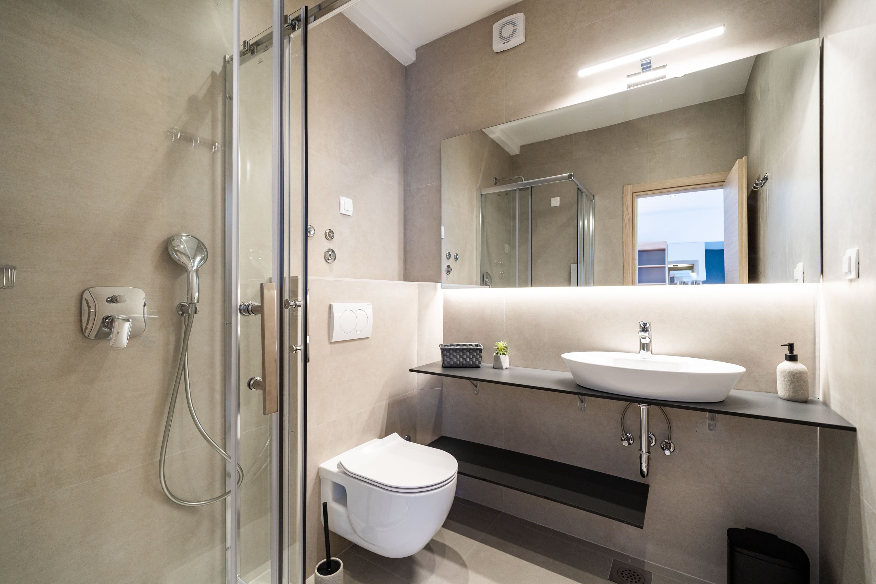 Une salle de bain moderne avec une douche à parois de verre, des toilettes blanches, un lavabo en verre et un grand miroir.